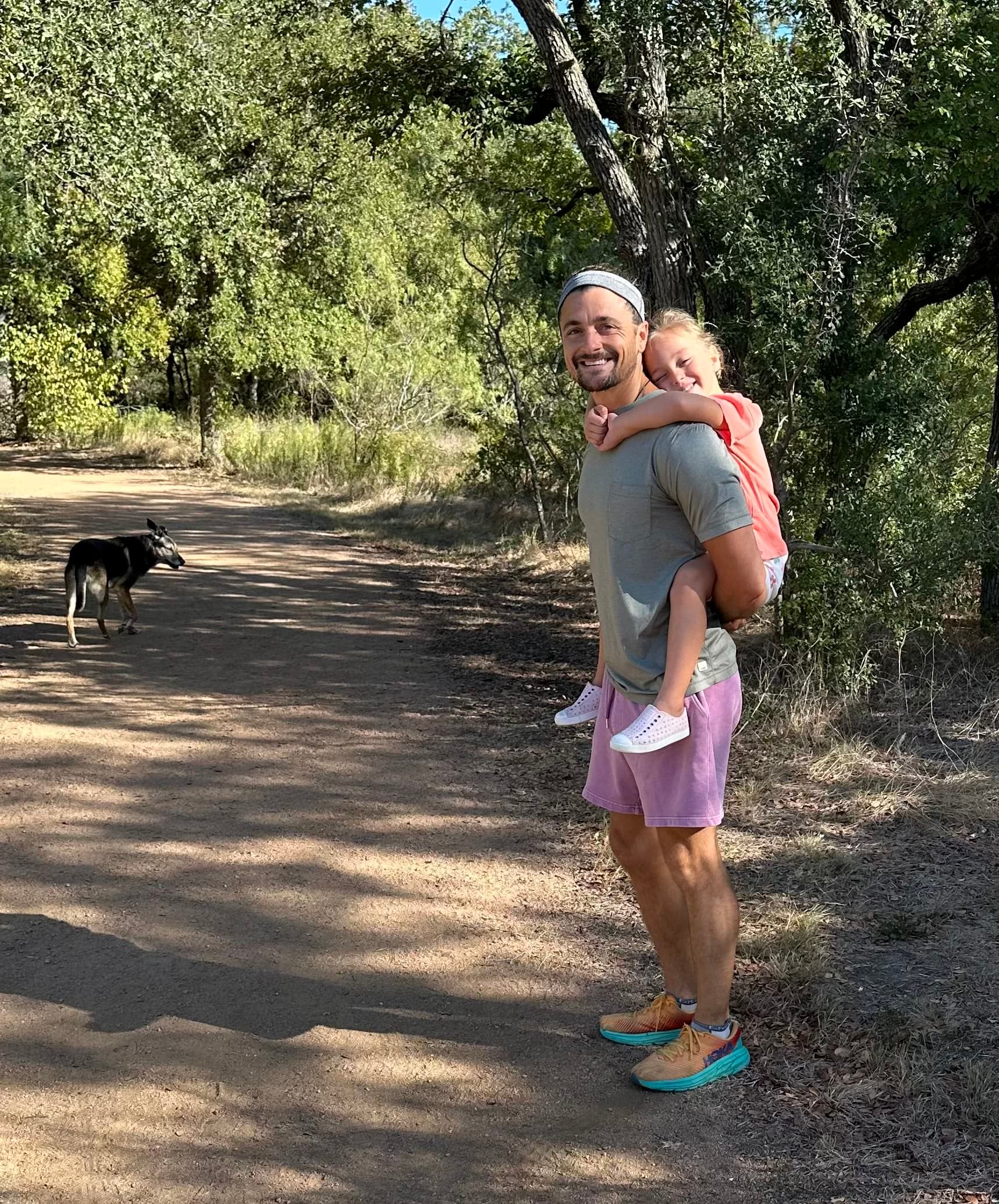 John Thomas carrying his daughter on a trail, dog running ahead